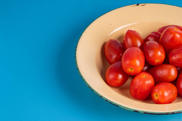 Skupina čerstvých cherry rajčat na rustikálním talíři izolátu v modrém pozadí. zavřít zásobník cherry rajčat na rustikální talíř. - Fotografie, Obrázek