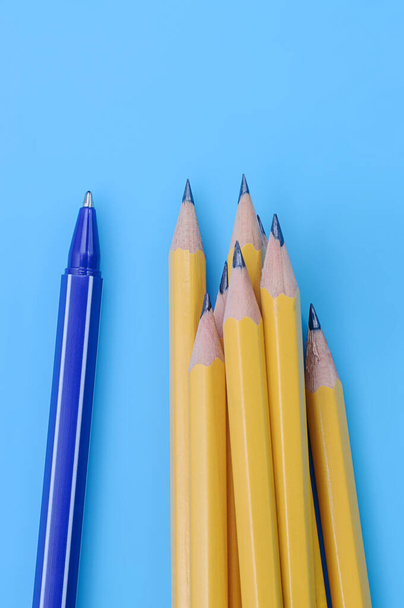 Una pluma azul y un grupo de lápices amarillos sobre fondo azul. Concepto de individualidad y diferencia. - Foto, imagen