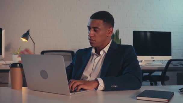 empresário afro-americano digitando no laptop e bebendo café para ir à noite - Filmagem, Vídeo