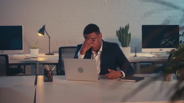 tired african american businessman touching eyes while typing on laptop at night - Footage, Video
