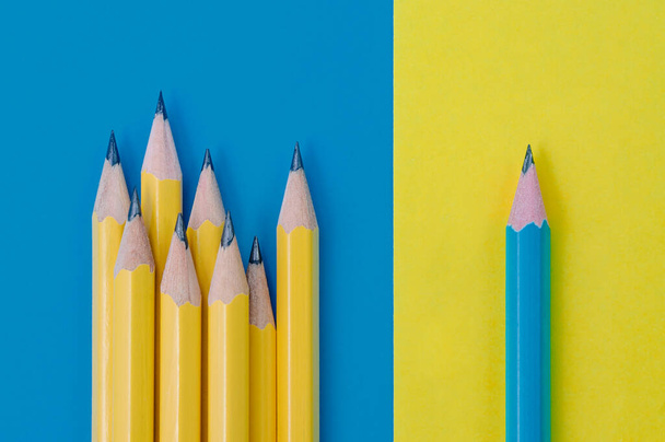 Jeden niebieski ołówek na żółtym tle i grupa żółtych ołówków na niebieskim tle. Pojęcie indywidualności i różnicy. - Zdjęcie, obraz
