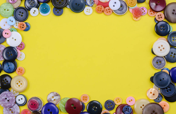 A pile of multicolored sewing buttons in the square shape on yellow background. Tailoring concept. Flat lay. Empty place for text. - Фото, изображение