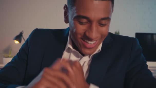 joyful african american businessman rubbing hands and eating donut in office - Footage, Video