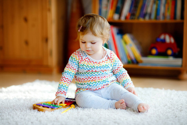 Little baby girl playing with educational wooden music toys at home or nursery. Toddler child with colorful wooden xylophon. Lonely kid during corona virus pandemic quarantine. - Foto, afbeelding