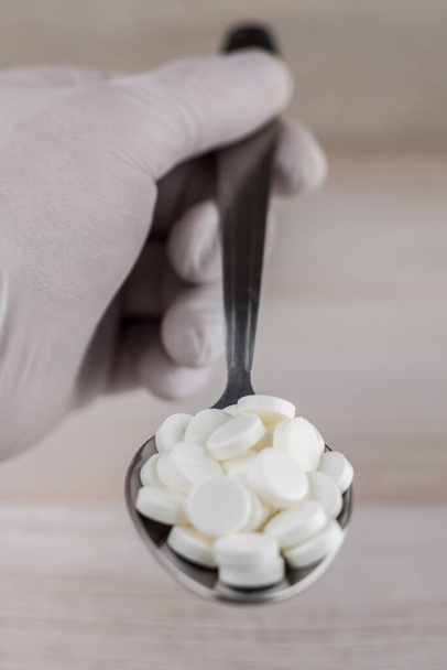 abuso de drogas médicas - el riesgo de sobredosis y muerte: muchas píldoras blancas en una cuchara mantienen a las personas guantes estériles - vista frontal - Foto, Imagen