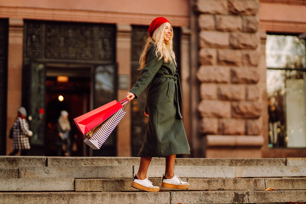 Stílusos fiatal modern nő divatos ruhákat színes bevásárló táskák sétál az utcán vásárlás után. Őszi bevásárlás. Fekete péntek.. - Fotó, kép