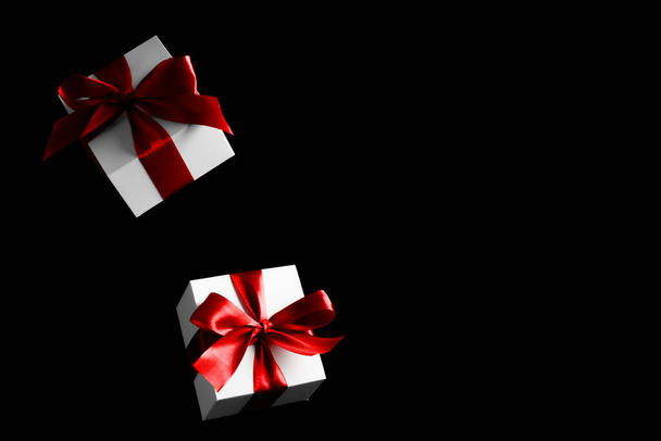 Present online. White gifts with red bow falling on black background for Black Friday banner. Flying backdrop with space for text - Fotoğraf, Görsel