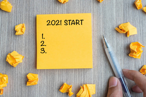 2021 Commencez mot sur mot jaune avec un homme d'affaires tenant un stylo et du papier émietté sur fond de table en bois. Nouvelle année, résolutions, stratégie et concept d'objectif - Photo, image