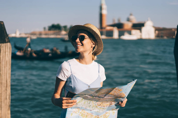 Happy woman in trendy outfit holding location paper map in hands and smiling during sightseeing tour near Grand Canal in romantic Italian city - Venezia,cheerful hipster girl enjoying European getaway - Foto, Bild