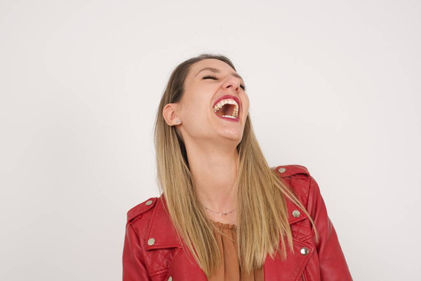 Радостная европейская женщина веселится и смеется над хорошей шуткой или поет в повседневной одежде, стоя у серой стены. Счастливая женщина с длинными волосами в помещении. - Фото, изображение