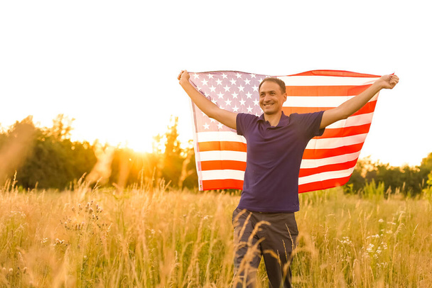 4 Ιουλίου. Πατριώτης με την εθνική αμερικανική σημαία στο πεδίο. Νεαρός άνδρας με υπερηφάνεια κυματίζει αμερικανική σημαία. Ημέρα ανεξαρτησίας. - Φωτογραφία, εικόνα