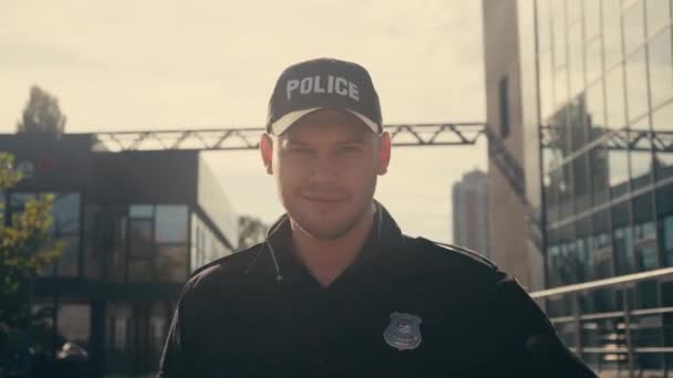 Policista se usmívá na kameru a dotýká se čepice na městské ulici  - Záběry, video