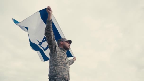 Laag hoekaanzicht van soldaat met vlag van Israël met lucht op de achtergrond  - Video