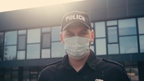 Politieagent in uniform en medisch masker kijkend naar camera buiten  - Video