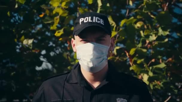 Dışarıda ağaçların yanında duran tıbbi maskeli bir polis.  - Video, Çekim