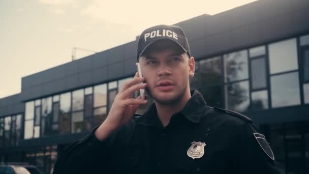 Policista v uniformě a čepice mluví na smartphone na městské ulici  - Záběry, video
