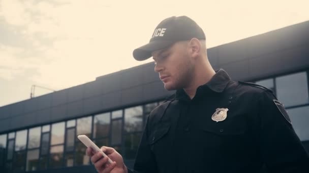 Fiatal rendőr okostelefont használ a városi utcán  - Felvétel, videó