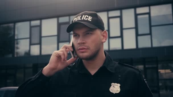 Politieagent in uniform en badge praten op smartphone in stedelijke straat  - Video