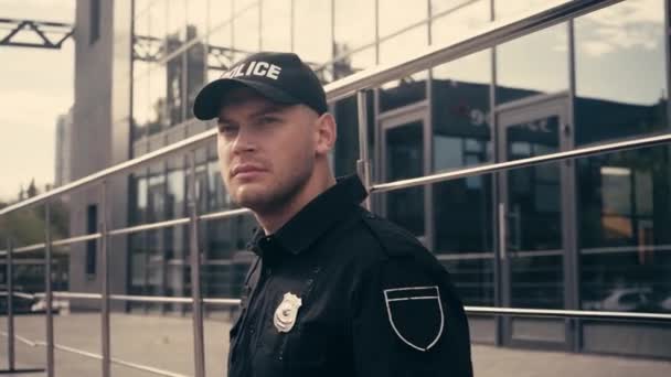 Νεαρός αστυνομικός με στολή στέκεται κοντά σε κιγκλίδωμα σε αστικό δρόμο  - Πλάνα, βίντεο