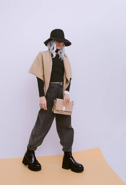 Model in studio wearing casual fall winter outfit. Fashion minimalistic lover. Details of everyday look. Trendy accessory hat, scarf and clutch bag. Stylish platform boots - Foto, Imagem