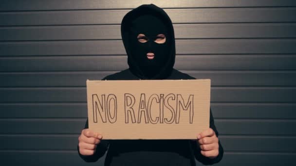 Giovane in passamontagna con cartello senza scritte razziste vicino all'edificio  - Filmati, video