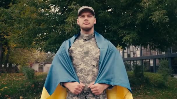 Soldier in uniform holding Ukrainian flag outdoors  - Footage, Video