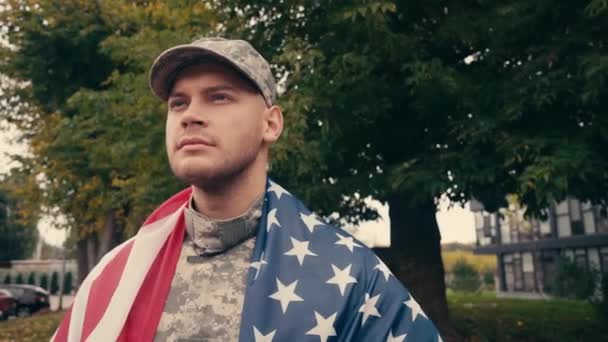 Soldado envuelto en bandera americana mirando al aire libre  - Imágenes, Vídeo