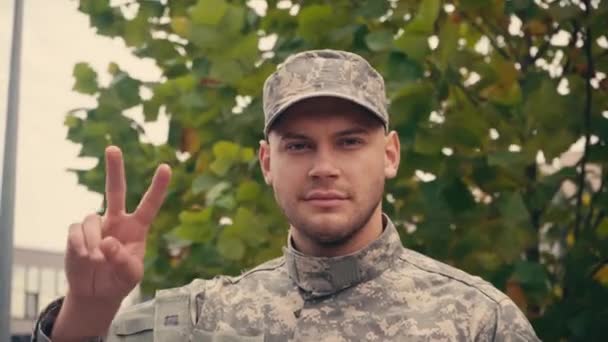 Giovane soldato in uniforme che mostra il segno della pace all'aperto - Filmati, video