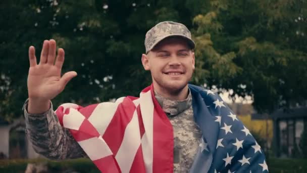 Веселый солдат с американским флагом машет рукой на городской улице  - Кадры, видео