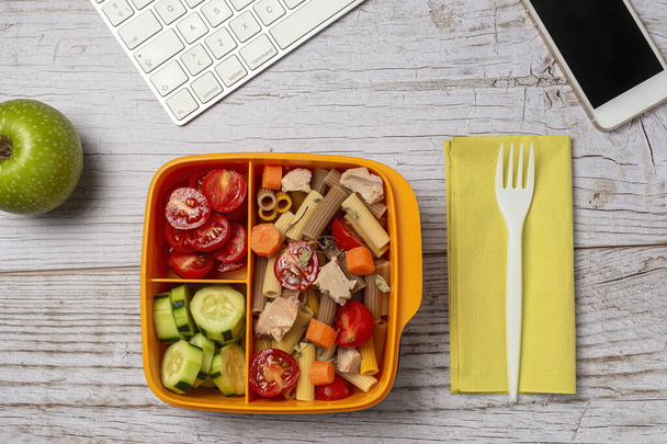 Lunch at work place healthy pasta with tuna, cherry tomatoes, carrot, cucumber in lunch box on work table. Home food for office concept - Фото, изображение