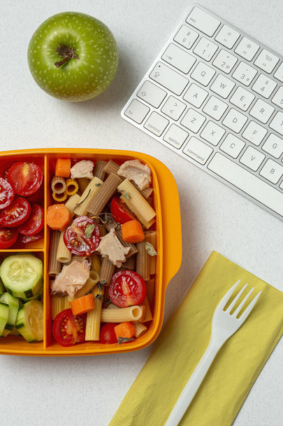 Lunch at work place healthy pasta with tuna, cherry tomatoes, carrot, cucumber in lunch box on work table. Home food for office concept - Photo, Image
