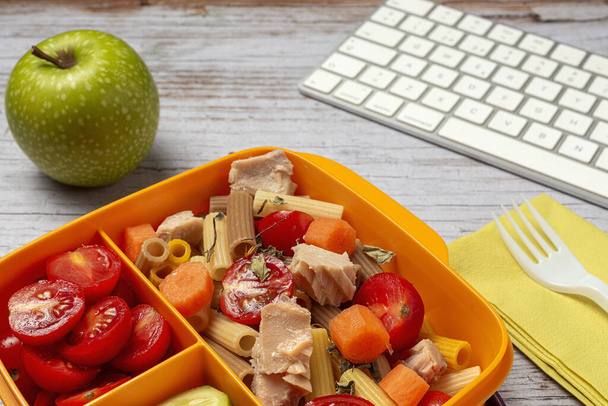 Lunch at work place healthy pasta with tuna, cherry tomatoes, carrot, cucumber in lunch box on work table. Home food for office concept - Foto, imagen
