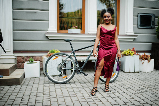 Portrait of a beautiful natural young African woman with afro hair. Black model in red silk dress with mountain bike. - Foto, imagen