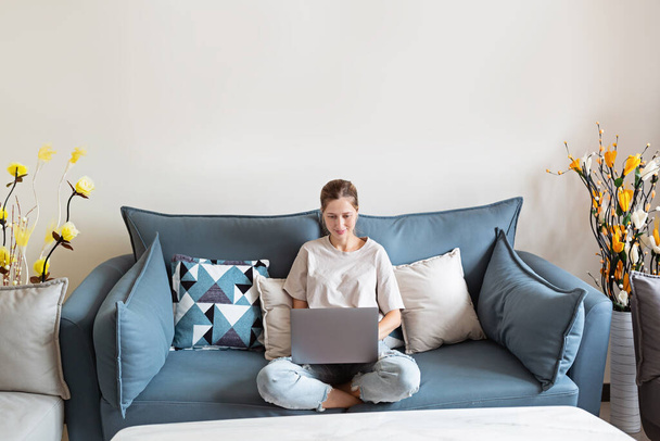 Young beautiful woman stylish wearing on gray textile sofa at home. Attractive slim female in domestic situation, staying home, resting on couch in her apartment. Background, copy space, close up. - 写真・画像