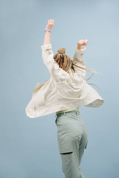 Celebrating young woman with stylish blond afro braids from behind over blue. Over blue background. Throwing hands in the air. - Fotoğraf, Görsel