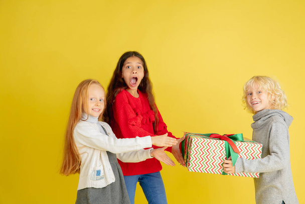 Giving and getting presents on Christmas holidays. Group of happy smiling children having fun isolated on yellow studio background - Valokuva, kuva