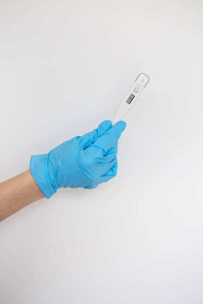 Ręka medyka nosi niebieską lateksową rękawicę trzymającą termometr, który pokazuje temperaturę ciała pacjenta na niebieskim tle. Grypa, koncepcja choroby - Zdjęcie, obraz