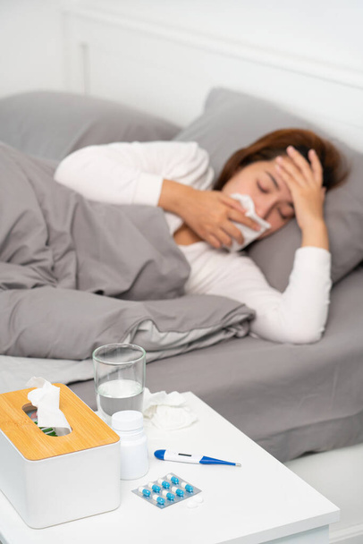 pílula e copos de água na mesa mulher que sofre de dor de cabeça, febre e gripe deitada no fundo da cama. - Foto, Imagem