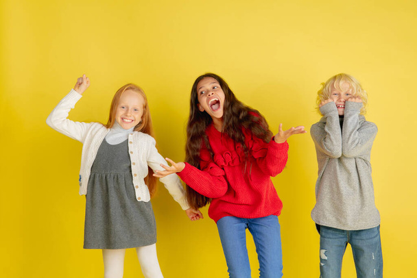 Portrait of little caucasian children with bright emotions isolated on yellow studio background - Photo, Image