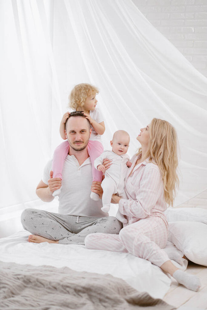 A young Caucasian family with two children daughters in a white home interior. Home clothes. - 写真・画像