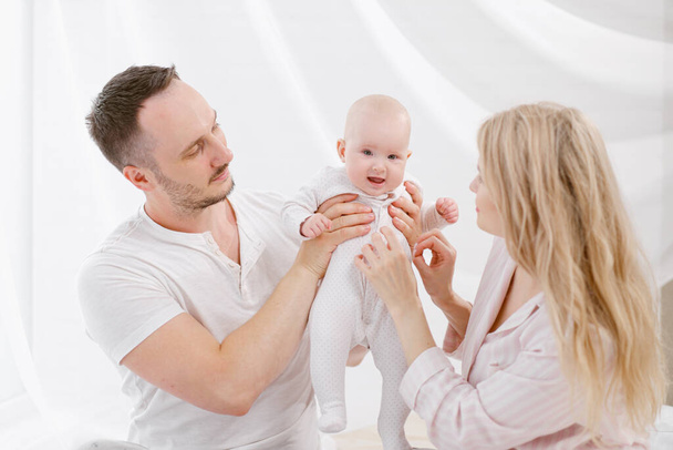 A young Caucasian family with a newborn baby daughter in the bedroom. White light home interior. - Photo, Image