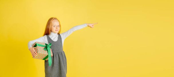 Giving and getting presents on Christmas holidays. Teen girl having fun isolated on yellow studio background - Foto, afbeelding