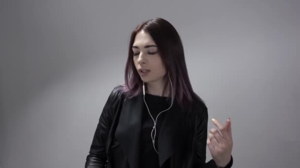 Portret van dansende jonge dame in oordopjes op de witte achtergrond in slowmo - Video