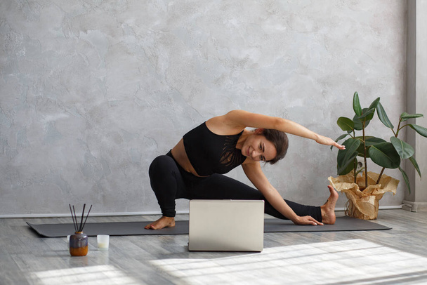 Młoda sportowa instruktorka jogi trenuje online, nagrywając lekcje jogi na laptopie. Piękna kobieta ćwicząca jogę. Postawy jogi, medytacja, relaks, dobre samopoczucie i zdrowie - Zdjęcie, obraz