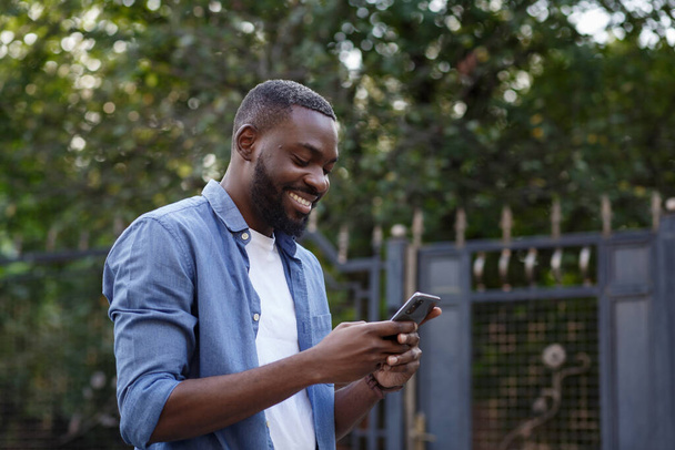 Happy man using mobile phone apps, texting message, browsing internet, looking at smartphone. Handsome Afro-American man using smartphone and smiling. Young people working with mobile devices - Fotoğraf, Görsel