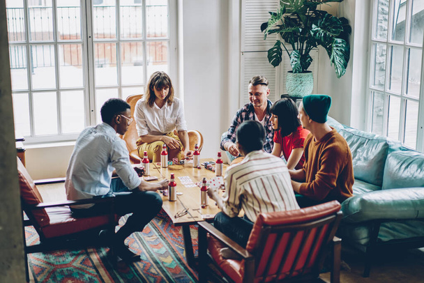 Trendy hipster guys feeling comfort during together weekend for practice blackjack skills, youthful group of young diverse players creating strategy for casino board games with cards and chips - 写真・画像