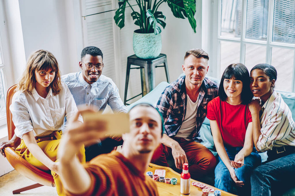 Group of diverse players looking at camera while photographing themself during weekend poker gaming, youthful hipsters enjoying leisure drinks meeting in cozy interior shooting vlog party video - Fotografie, Obrázek