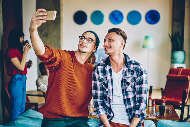 Handsome Caucasian male friends making together selfie content using smartphone front camera and filter application, youthful hipster guys posing for shooting influence video vlog during leisure time - Photo, Image