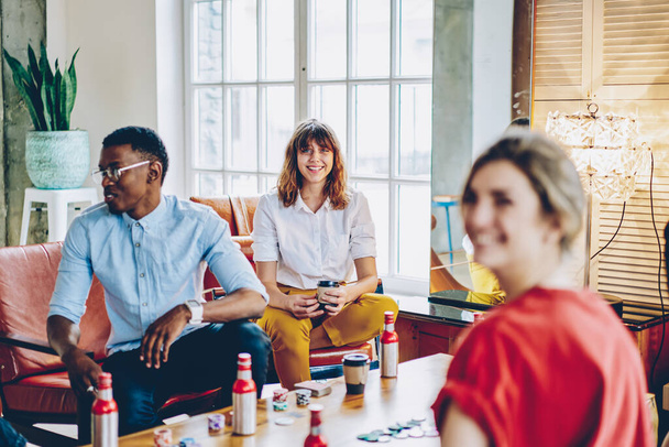 Portrait of cheerful Caucasian woman smiling at camera during positive gather meeting with best friends, happy millennial hipsters laughing during poker party with beer in loft home apartment - Foto, Imagem