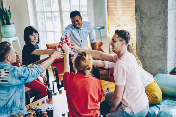 Happy multicultural people dressed in casual wear clicking with alcohol drinks celebrating friendly bonding meeting party for playing poker or blackjack game in modern home apartment, Cheers! - 写真・画像